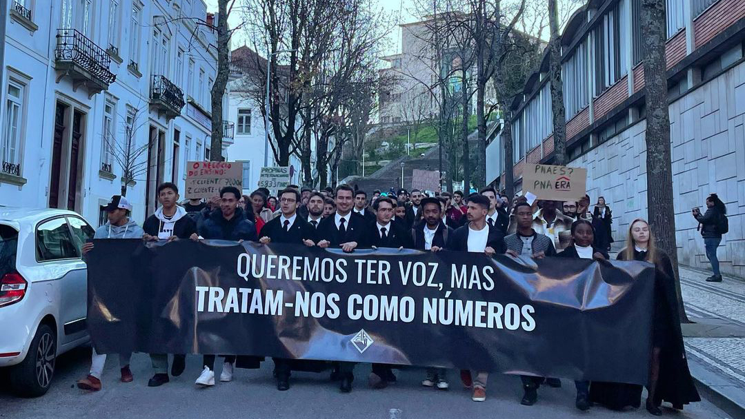 Picture of a crowd of students protesting for international students' rights, holding a large banner with an impactful sentence.